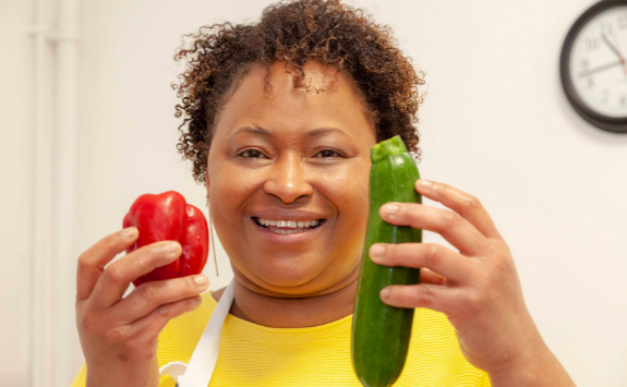Maria smiles into the camera holding a pepper and courgette	